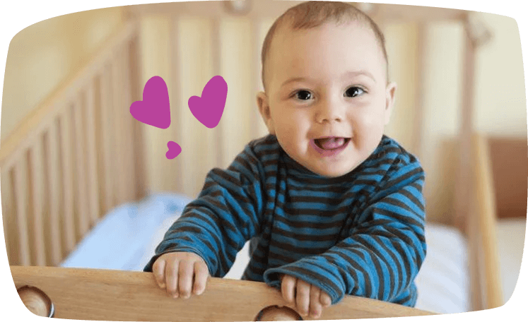 baby staat in ledikant en kijkt lachend naar de camera